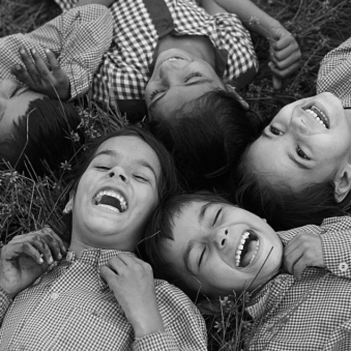 Group of cheerful children wearing school uniform lying down on grass & laughing elevated view.